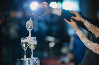 Cropped hands of newlywed couple pouring wine in glasses at wedding ceremony