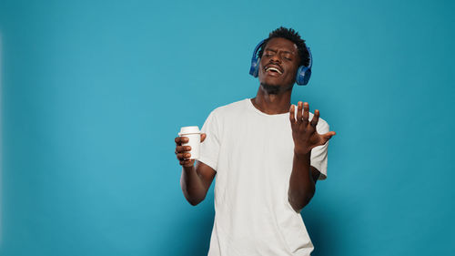 Man wearing headphones while standing against blue background