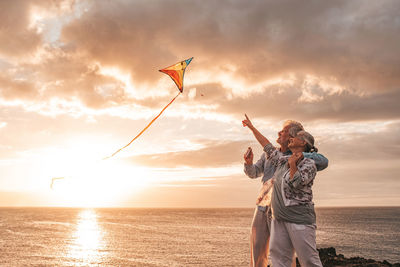 Senior couple flying kite while standing at beach against sky