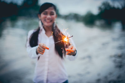 Cheerful woman holding lit sparklers at lakeshore