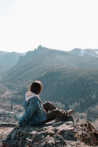 Rear view of woman sitting on mountain against sky