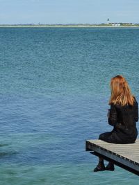 Rear view of woman sitting on pier over sea against sky