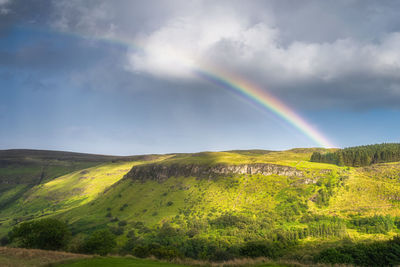 Vivid rainbow over hills and forests covered in patches of sunlight, glenariff forest park