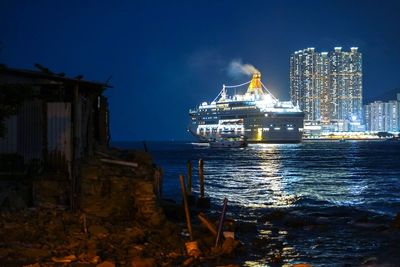 Illuminated buildings by sea against sky at night