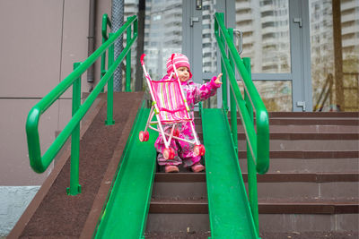 Toddler drags a toy stroller along the ramp of the stairs