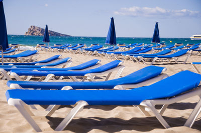 Blue lounge chairs at beach against sky on sunny day