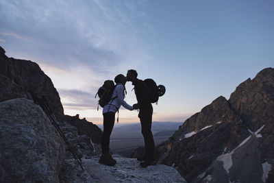 Two hikers with backpacks kiss at sunrise in the mountains, wyoming