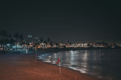 Illuminated city by sea against clear sky at night