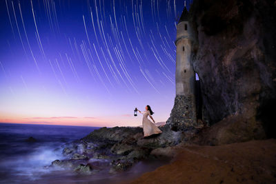 Man standing on rock by sea against sky at night