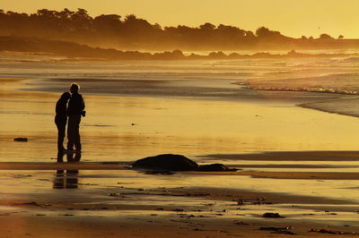 Man and woman standing at beach during sunset