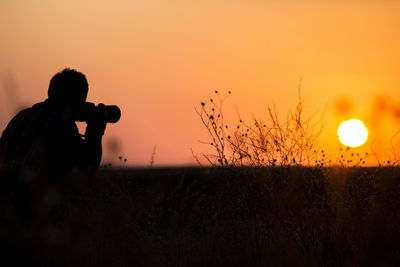 Silhouette man photographing on field against orange sky