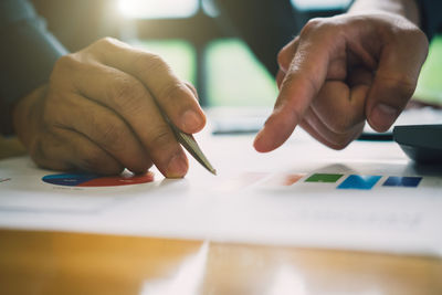 Cropped hands of colleagues discussing graphs on desk in office