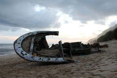 Abandoned boat on beach against sky during sunset