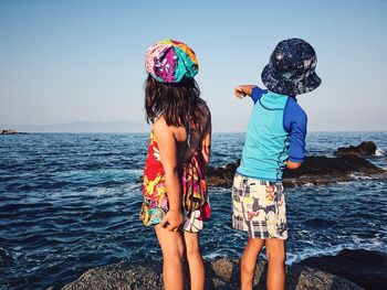 Rear view of children on shore at beach against sky