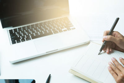 High angle view of cropped hands writing on diary at desk in office