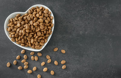 Appetizing dry cat food in a heart-shaped bowl on a dark background.