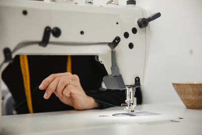 Adult woman sitting at table and making garment part on sewing machine while working in professional studio