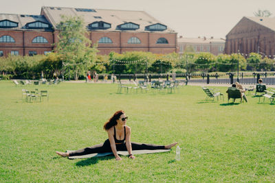Full length of woman wearing sunglasses exercising on mat in park