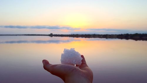 Close-up of hand holding salt against sky during sunset