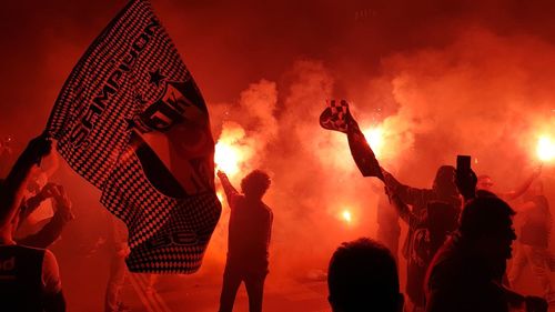 People with fire crackers against sky at night