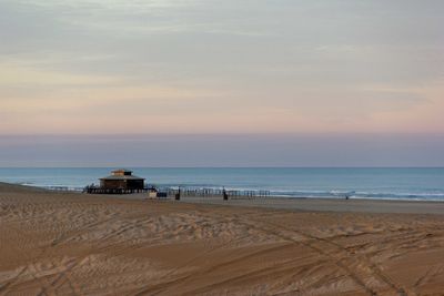 Scenic view of sandy beach with tire tracks at sunset