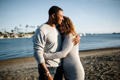 Multi racial couple embrace on beach at sunset