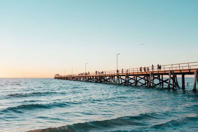 Pier over sea against clear sky at sunset