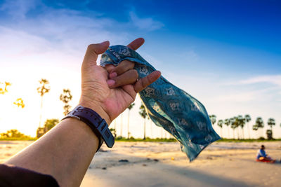 Close-up of hand holding fabric while gesturing at beach against sky