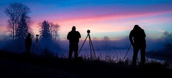 Silhouette people photographing on shore against sky during sunset