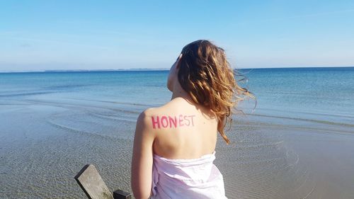 Rear view of woman with text on back at beach