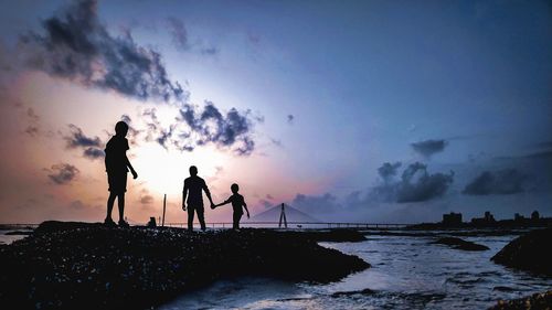 Silhouette people on beach against sky during sunset