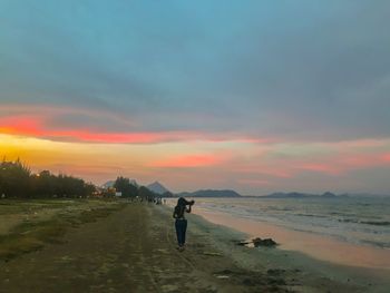 Man standing on beach against sky during sunset