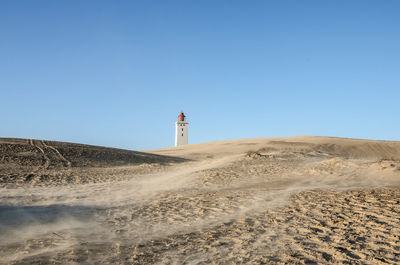 Lighthouse on beach against clear blue sky