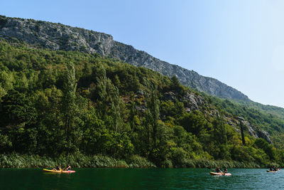 People sailing on sea by mountains against clear sky