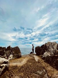 Man standing on rock looking at sea against sky