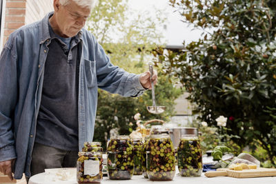 Senior man preparing olives in jars on table at back yard