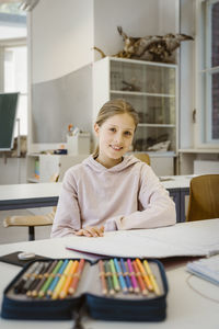 Portrait of smiling schoolgirl sitting at desk in classroom