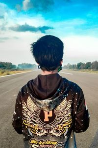 Rear view of boy standing on road against sky