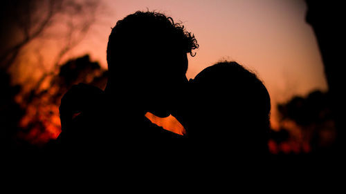 Silhouette man and woman kissing against sky during sunset