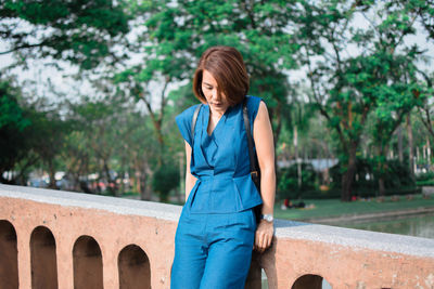 Woman leaning on railing against trees