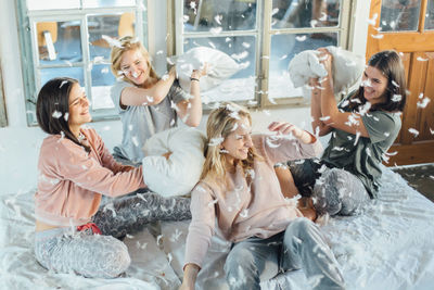 High angle view of cheerful friends playing pillow fight on bed at home