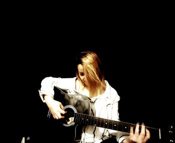 Young woman playing guitar against black background