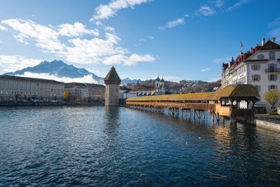 Bridge over river by buildings against sky