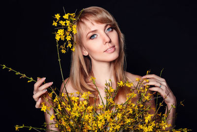 Portrait of beautiful young woman holding yellow flower against black background