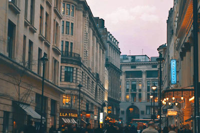 Illuminated street amidst buildings against sky at dusk