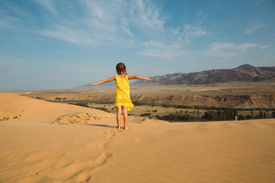 Rear view of woman standing on sand at desert