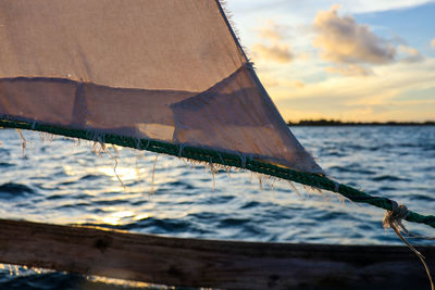 Close-up of sailboat sailing on sea against sky during sunset