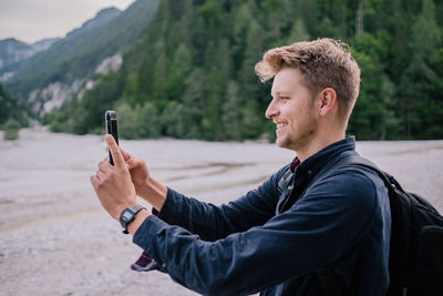 Side view of young man using mobile phone while standing on land