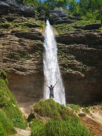 Rear view of man with arms raised against waterfall