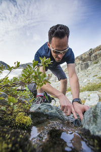 Low angle of active man filling water bottle from mountain stream.